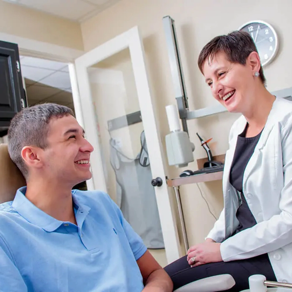 Dentist in light blue scrubs consulting with male patient in modern dental office treatment room.