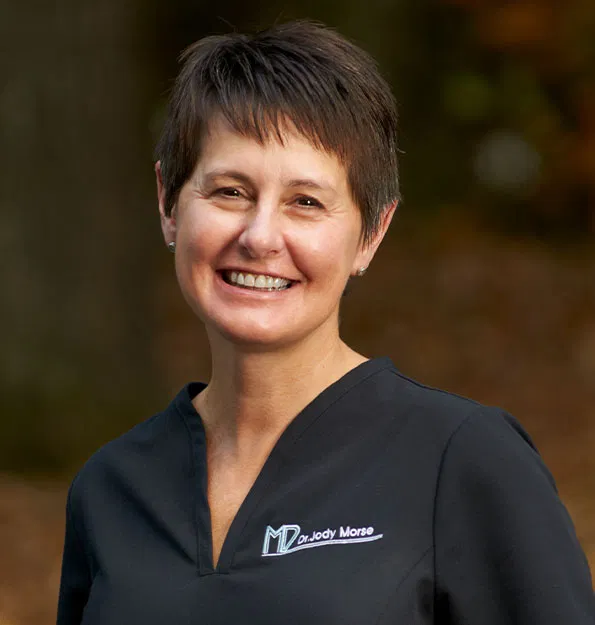 Professional woman in dark scrubs smiling at dental office.