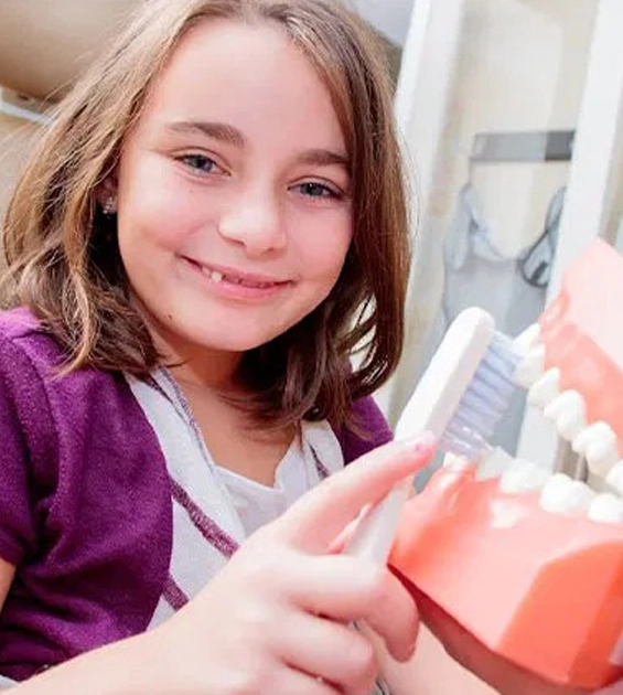 Young girl smiling while holding dental model in modern dental office setting.