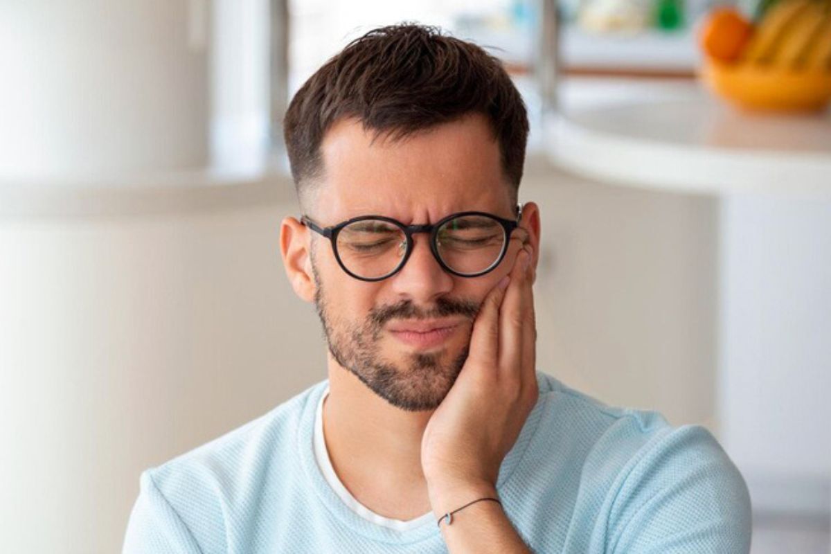 Man with glasses holding his cheek in pain, showing signs of dental discomfort or wisdom tooth problems.