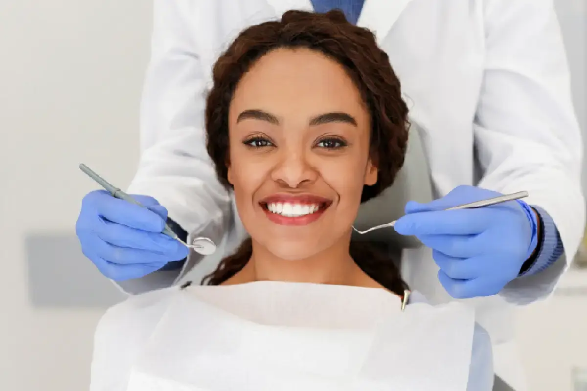 Smiling patient with dentist holding dental instruments during examination at Kernersville dental practice.