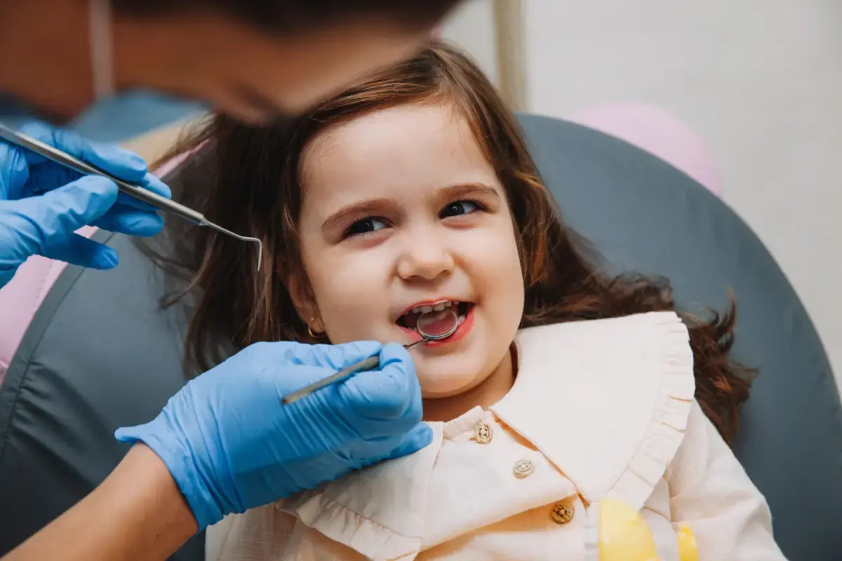 Young girl smiling during dental examination with dentist using instruments in clinical setting.
