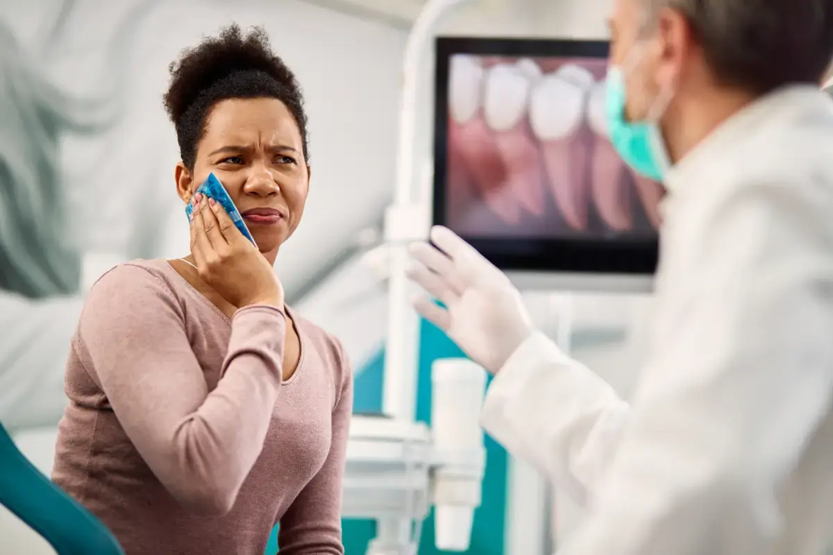 Woman with jaw pain holding her cheek during dental consultation with dentist.
