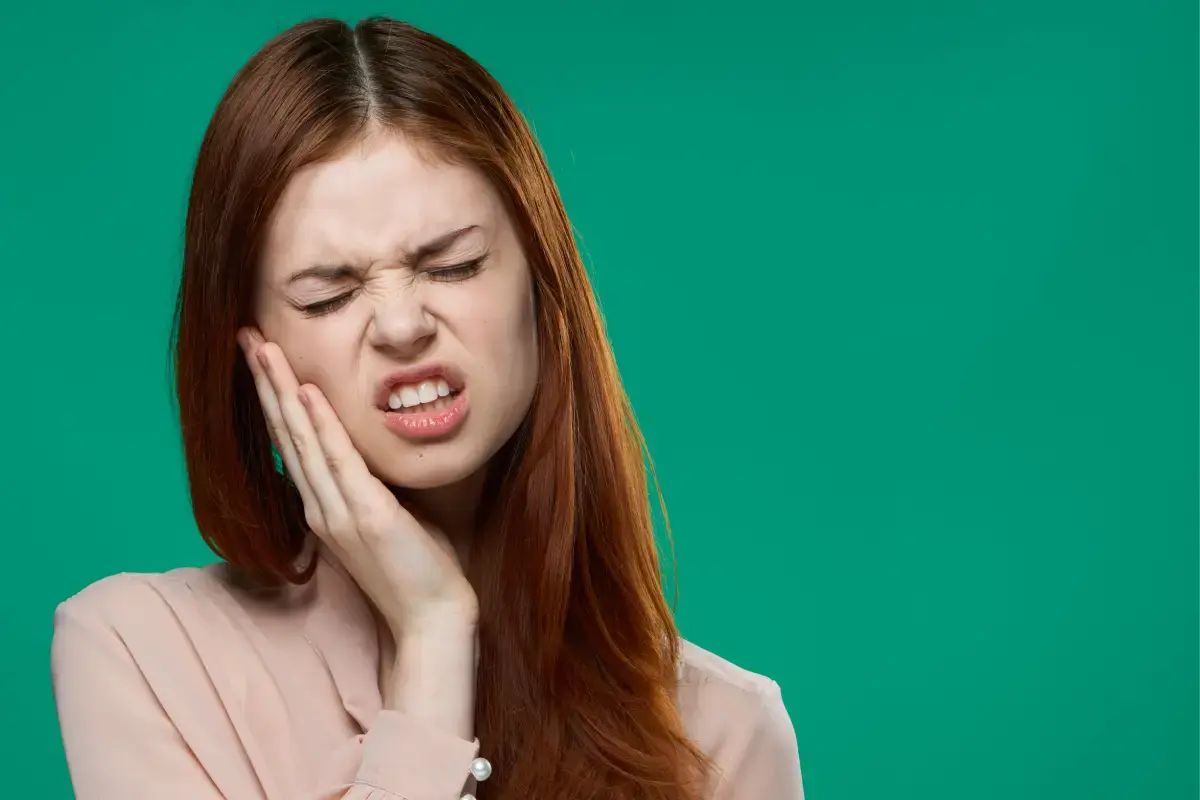 Woman with reddish-brown hair touching her cheek in pain, experiencing jaw or tooth discomfort related to TMJ disorder.