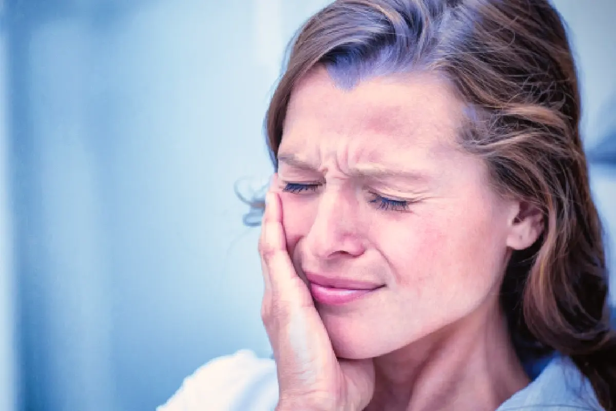 Woman experiencing dental pain, holding her cheek in discomfort.